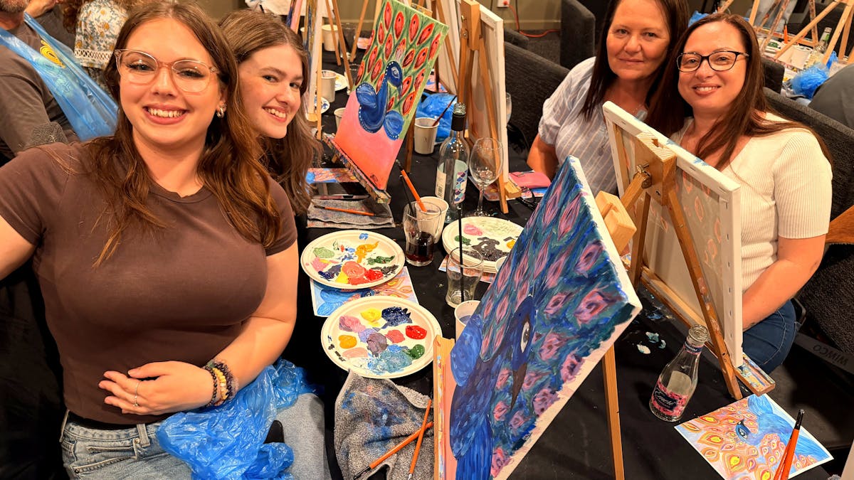 Group of Paint Juicy guests holding their finished peacock paintings at a mobile paint and sip event
