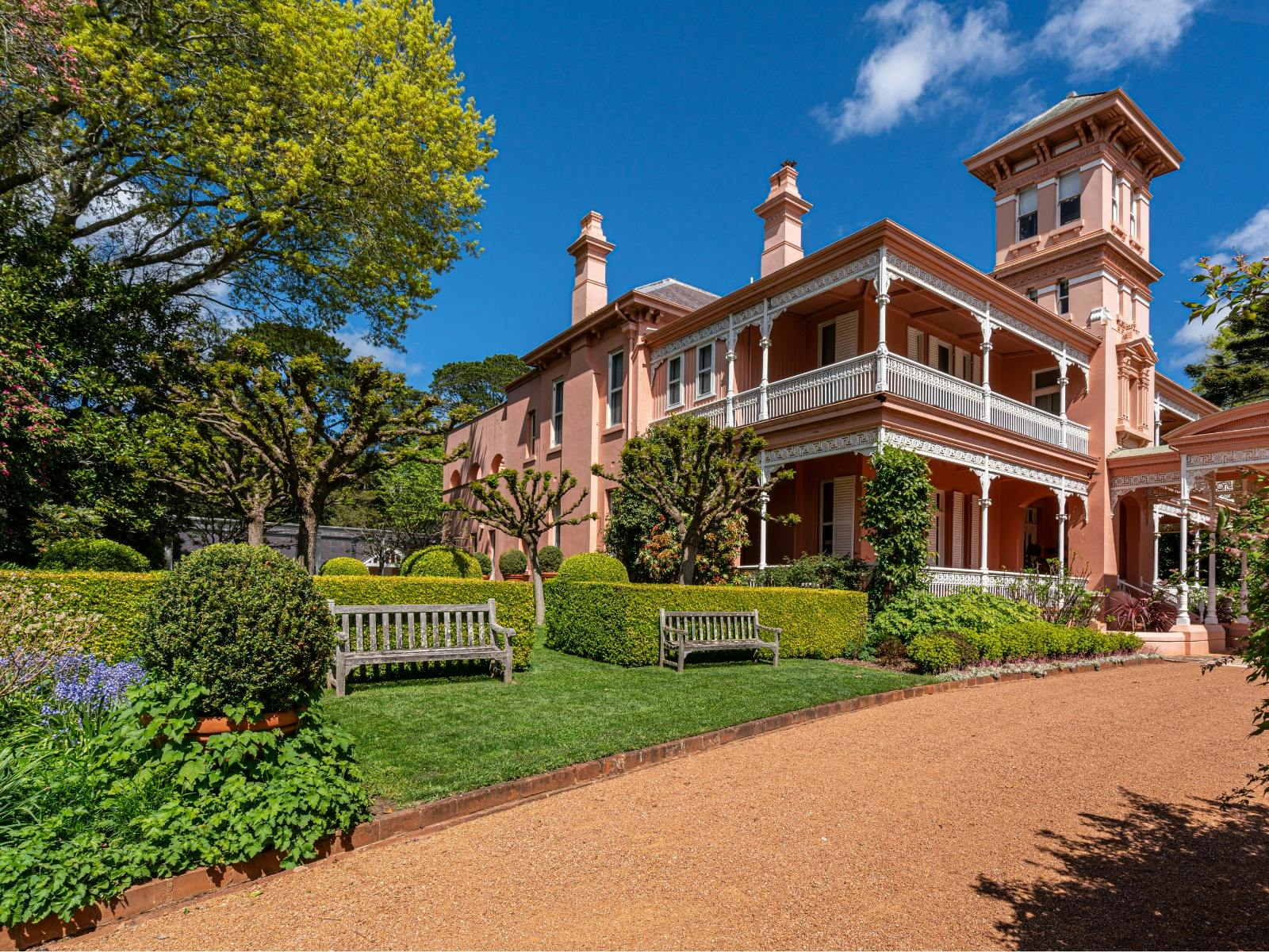 Pink mansion stands proudly with hedges, trees and flowers in spring bloom.