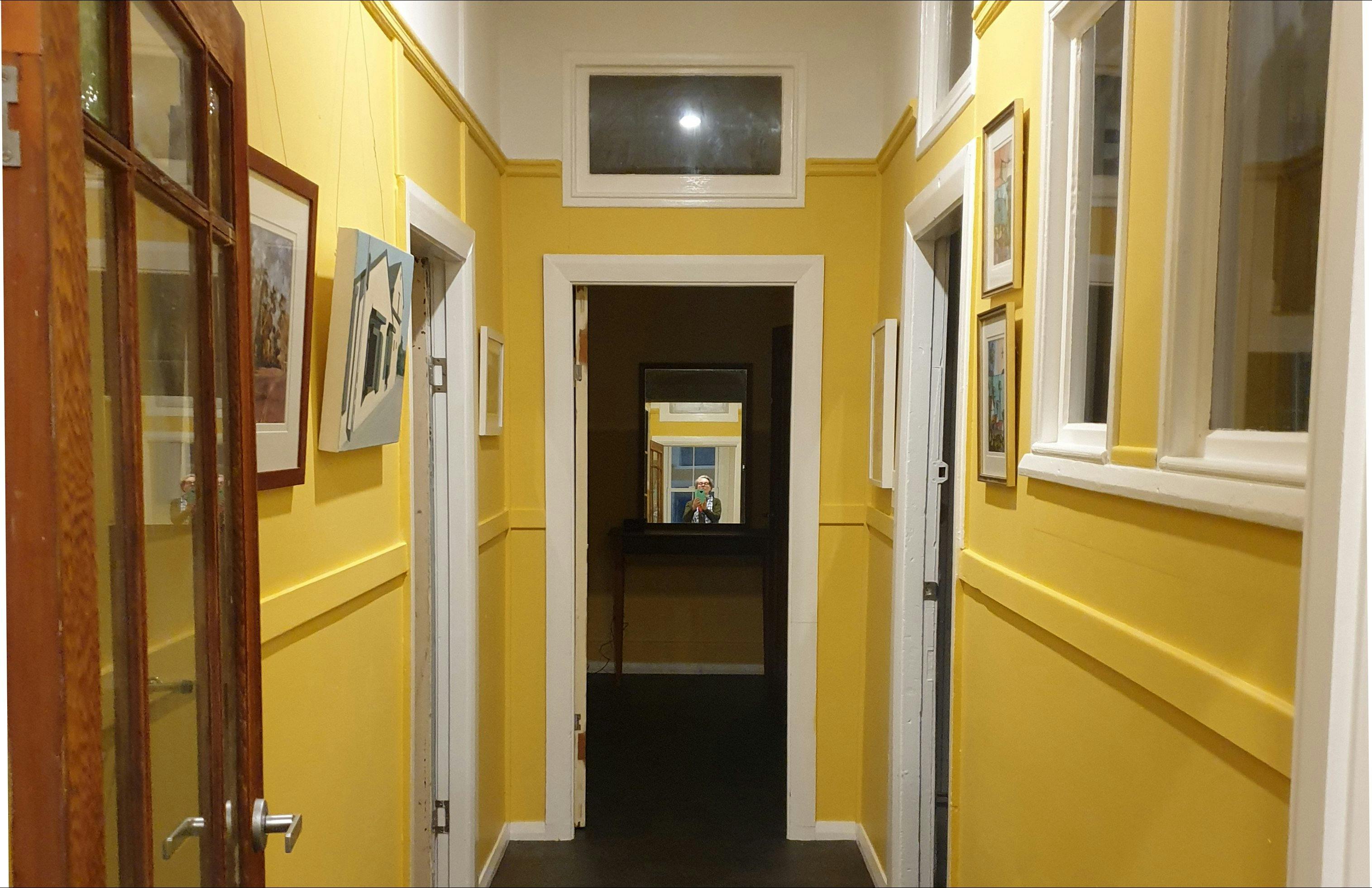Hallway, walls painted yellow with white trim, and paintings