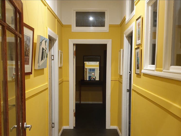 Hallway, walls painted yellow with white trim, and paintings