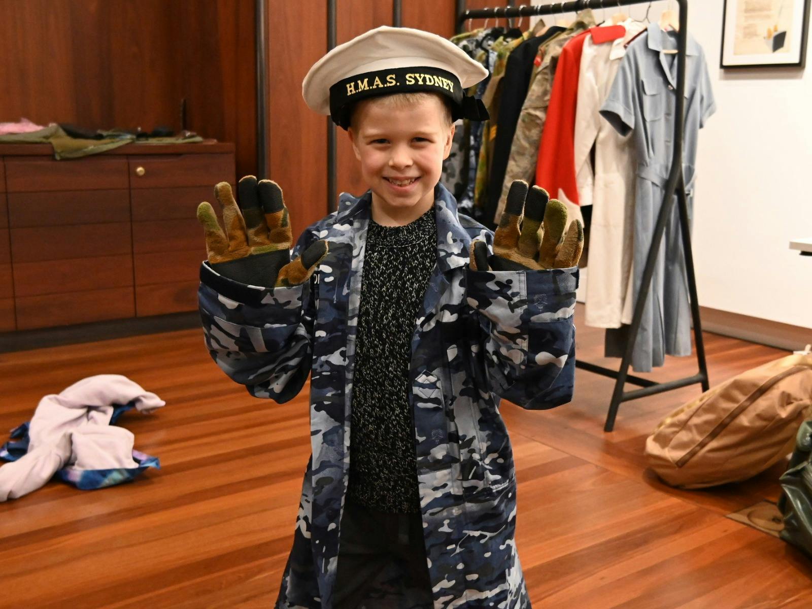 A child wearing a Royal Australian Navy  hat, camouflage gloves, and blue camouflage print shirt