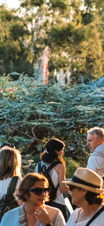 A bustling crowd outdoors at sunset. Tents and trees are visible,