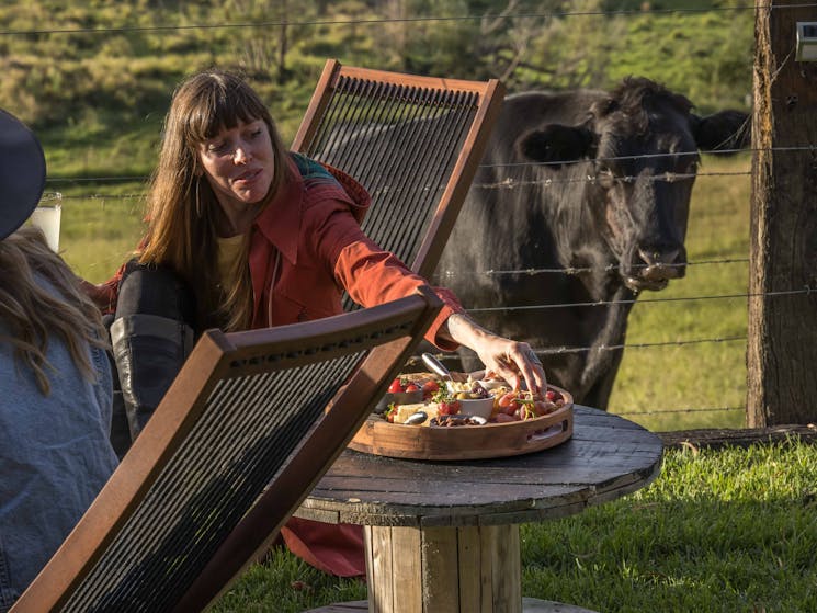 Women reaches for picnic while black cow watches her from behind