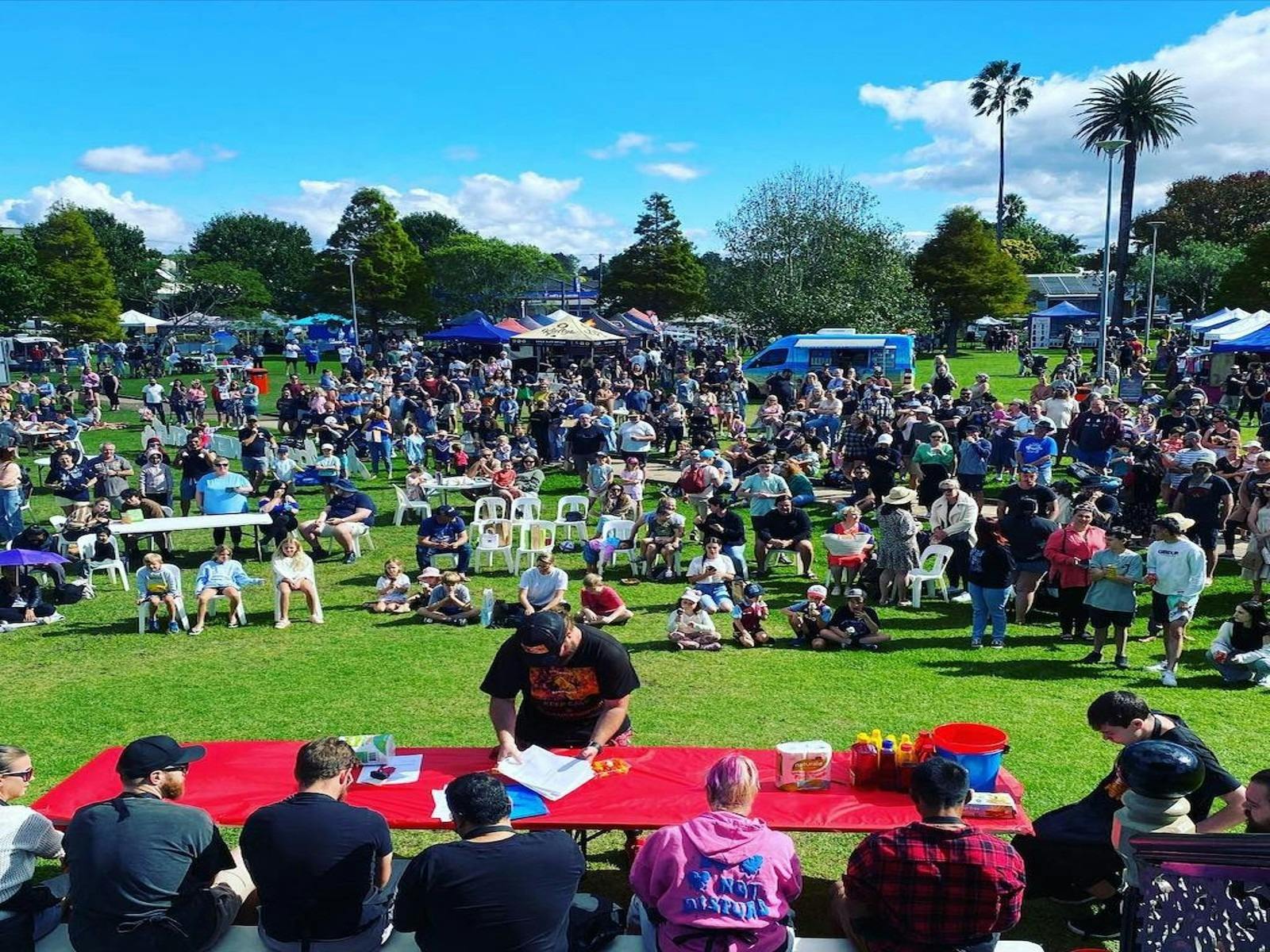 Large crowd gathered at an outdoor chilli festival watching a chilli eating competition with food st
