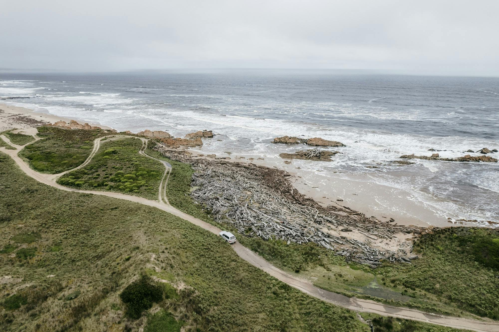 Aerial view of a winding off road 4WD track along the coast with the sea crashing against the coast