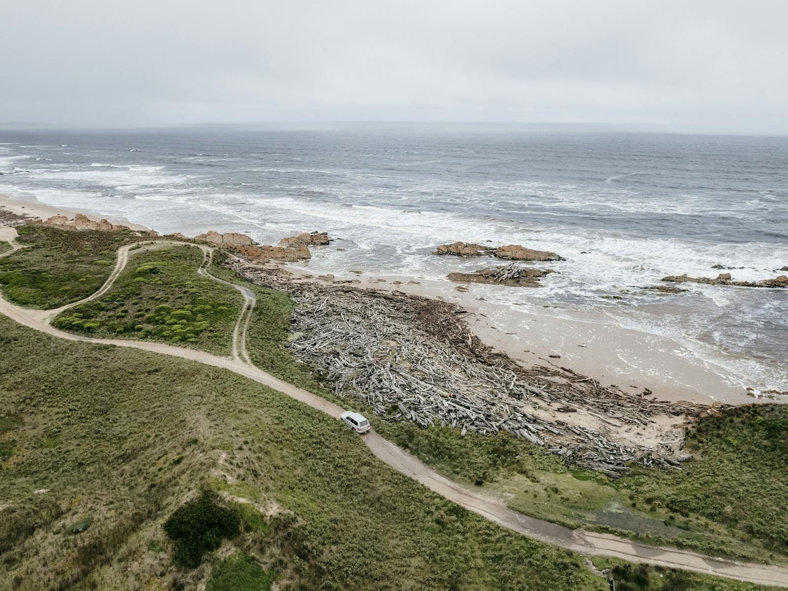 Aerial view of a winding off road 4WD track along the coast with the sea crashing against the coast