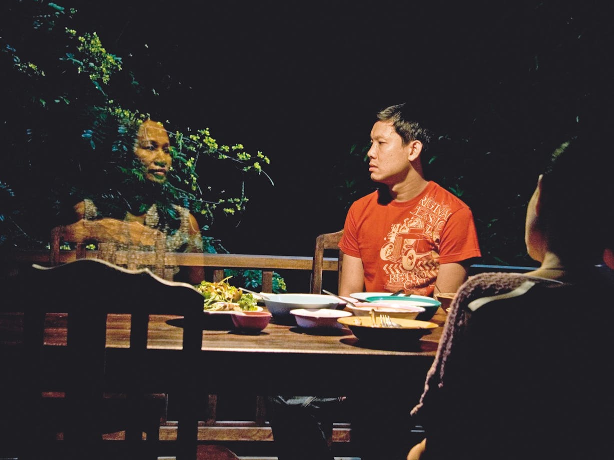 Man sitting around table at night with a ghost figure of a woman next to him