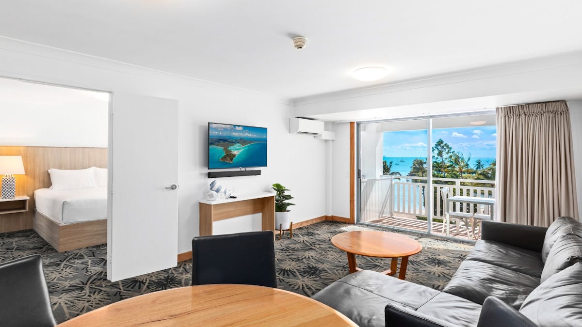Suite at Airlie Beach Hotel with separate lounge area, king bed, modern decor and oceanfront balcony