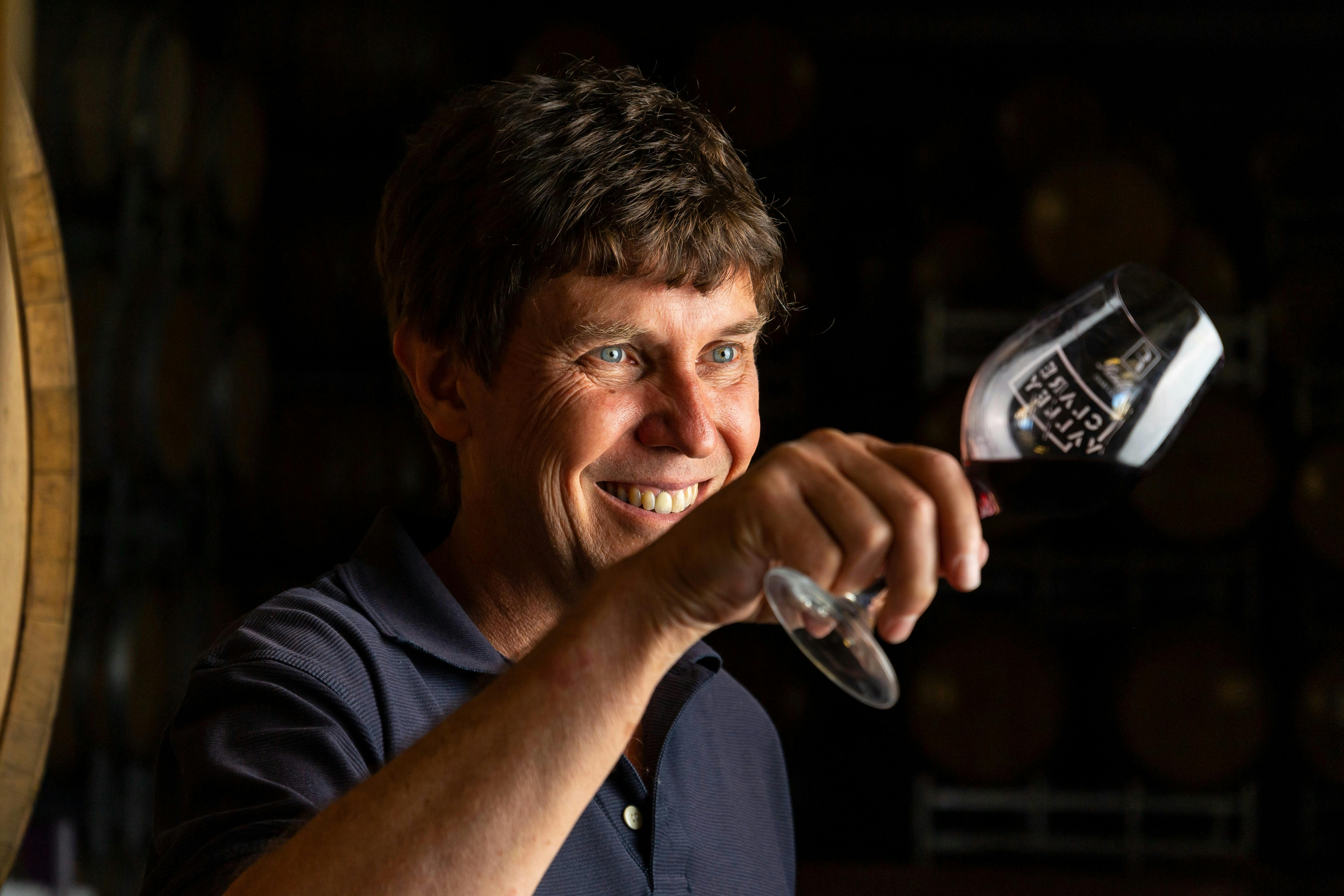 Man holding a wine glass on an angle smiling at it, black background