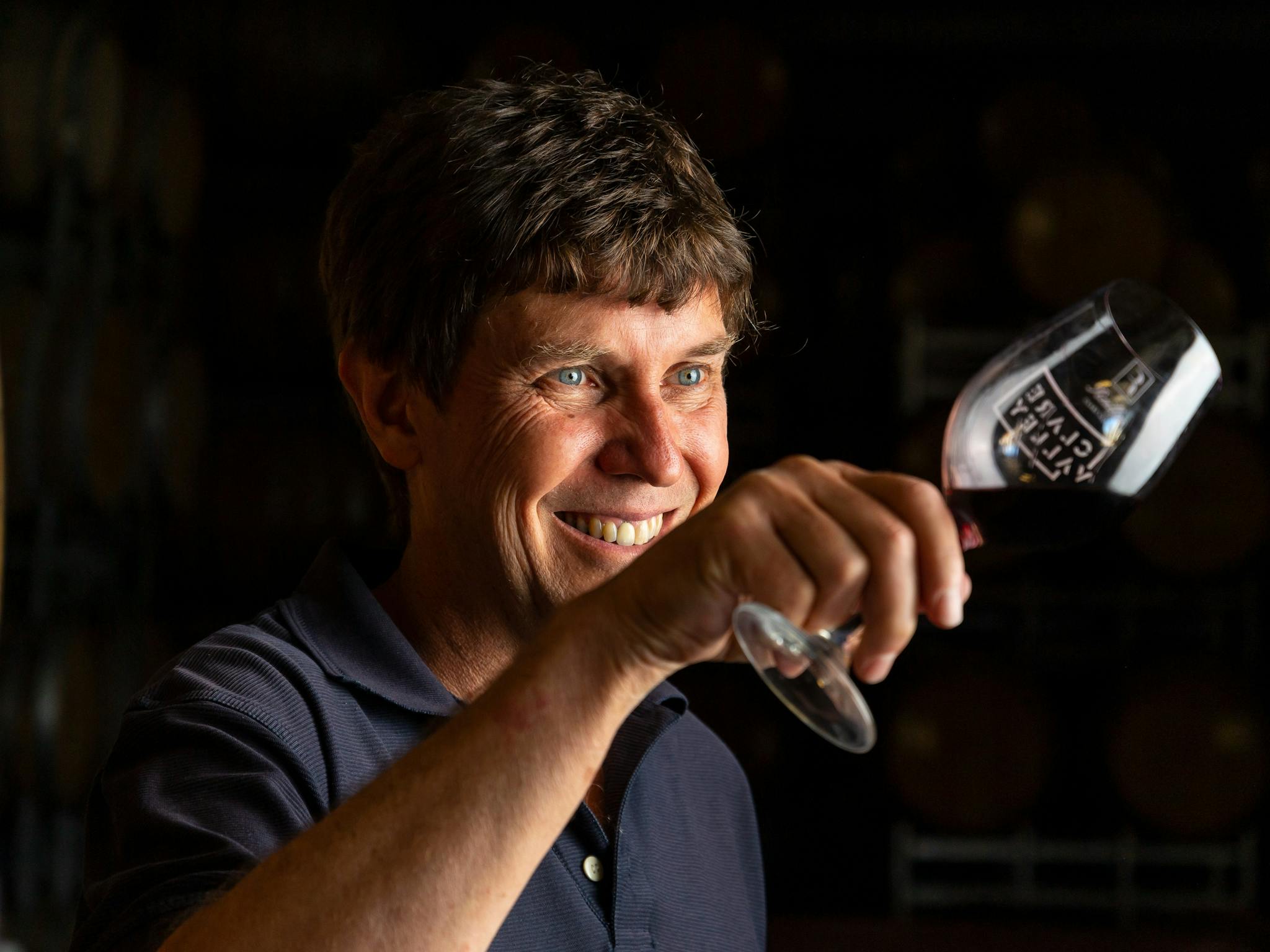 Man holding a wine glass on an angle smiling at it, black background