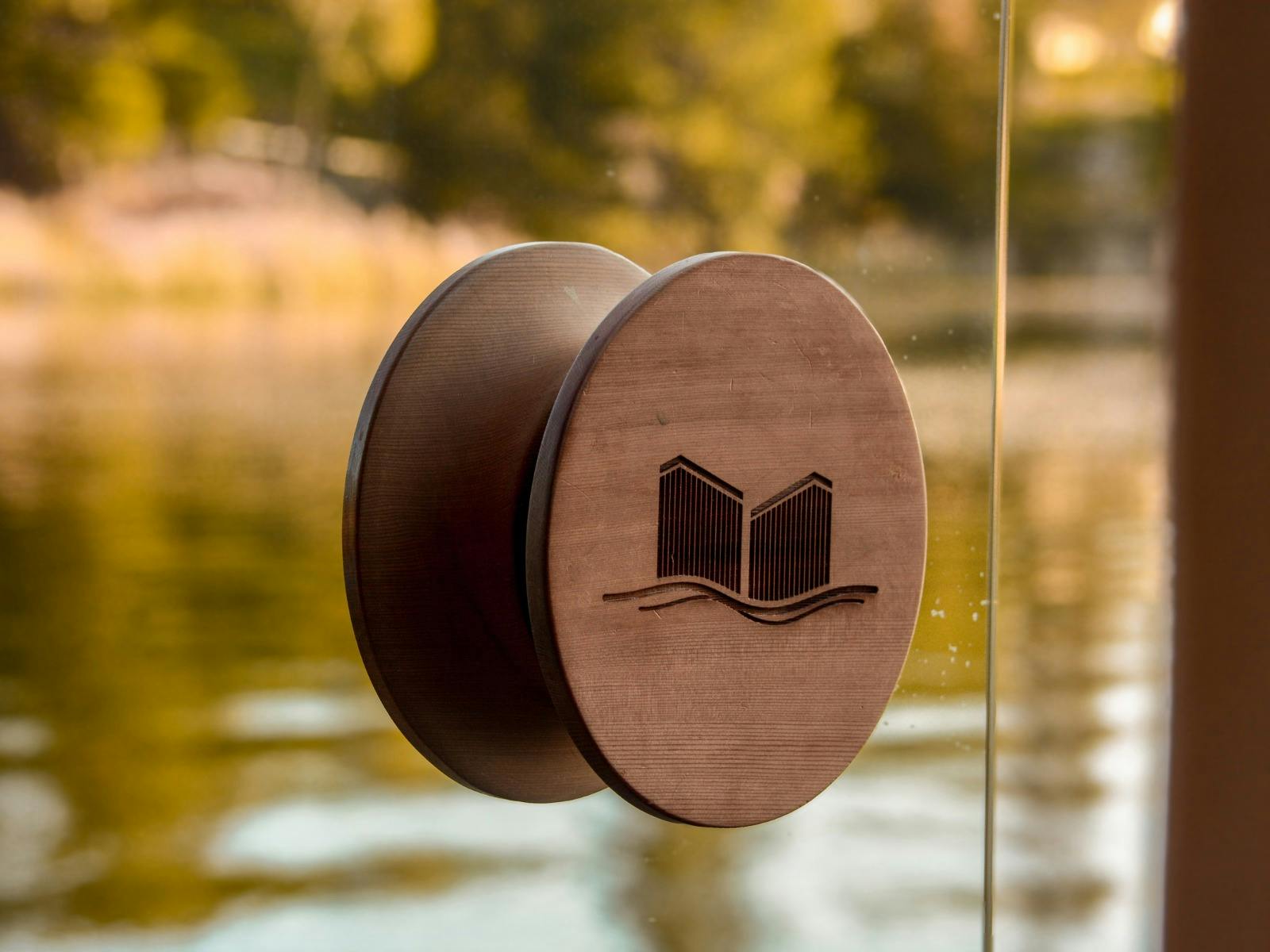 Detail of the Stillwater Saunas door handle featuring the logo, with the calm surface Lake Sambell