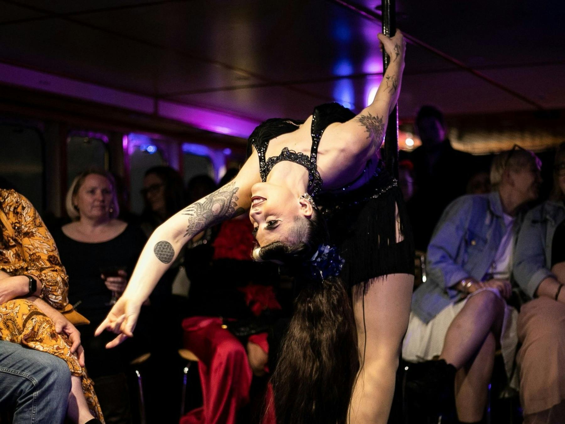 Juniper Fox performing a backbend on a pole fixture in front of the audience.