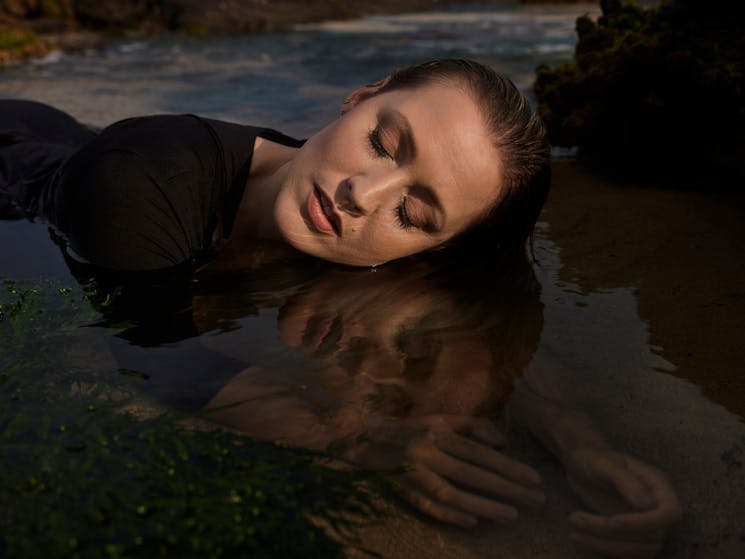 Model lying in a rock pool creating a mirror image.