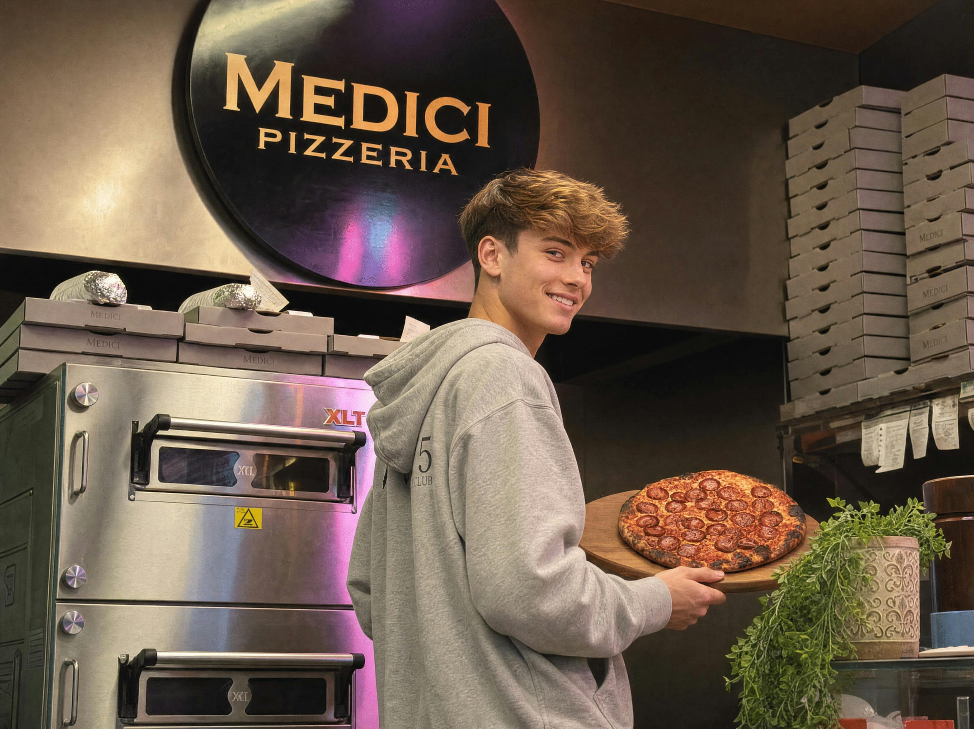 A Medici Pizzeria staff member holding a freshly              made pizza beside the oven