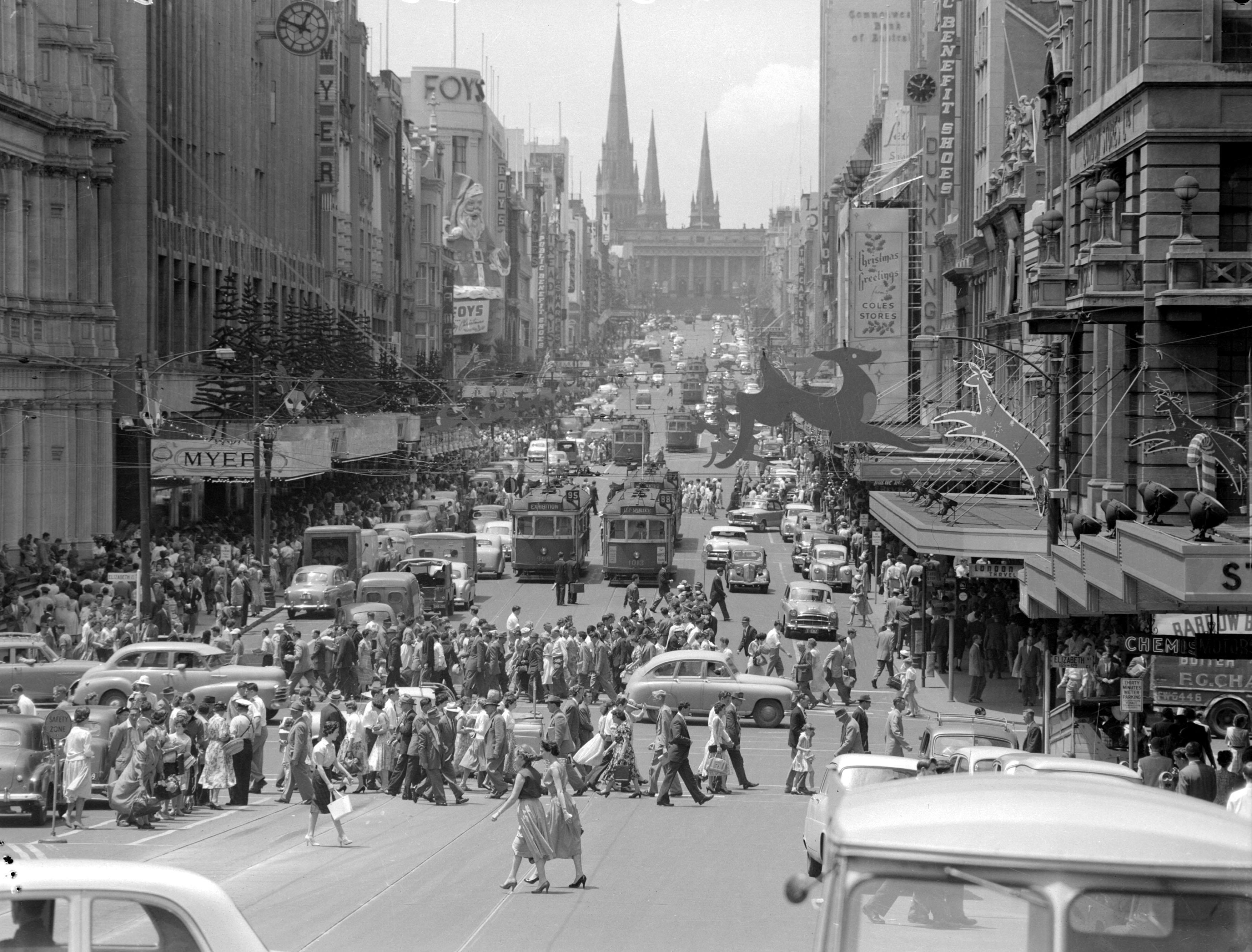 Busy street in a city. People cross the road while trams wait for them.