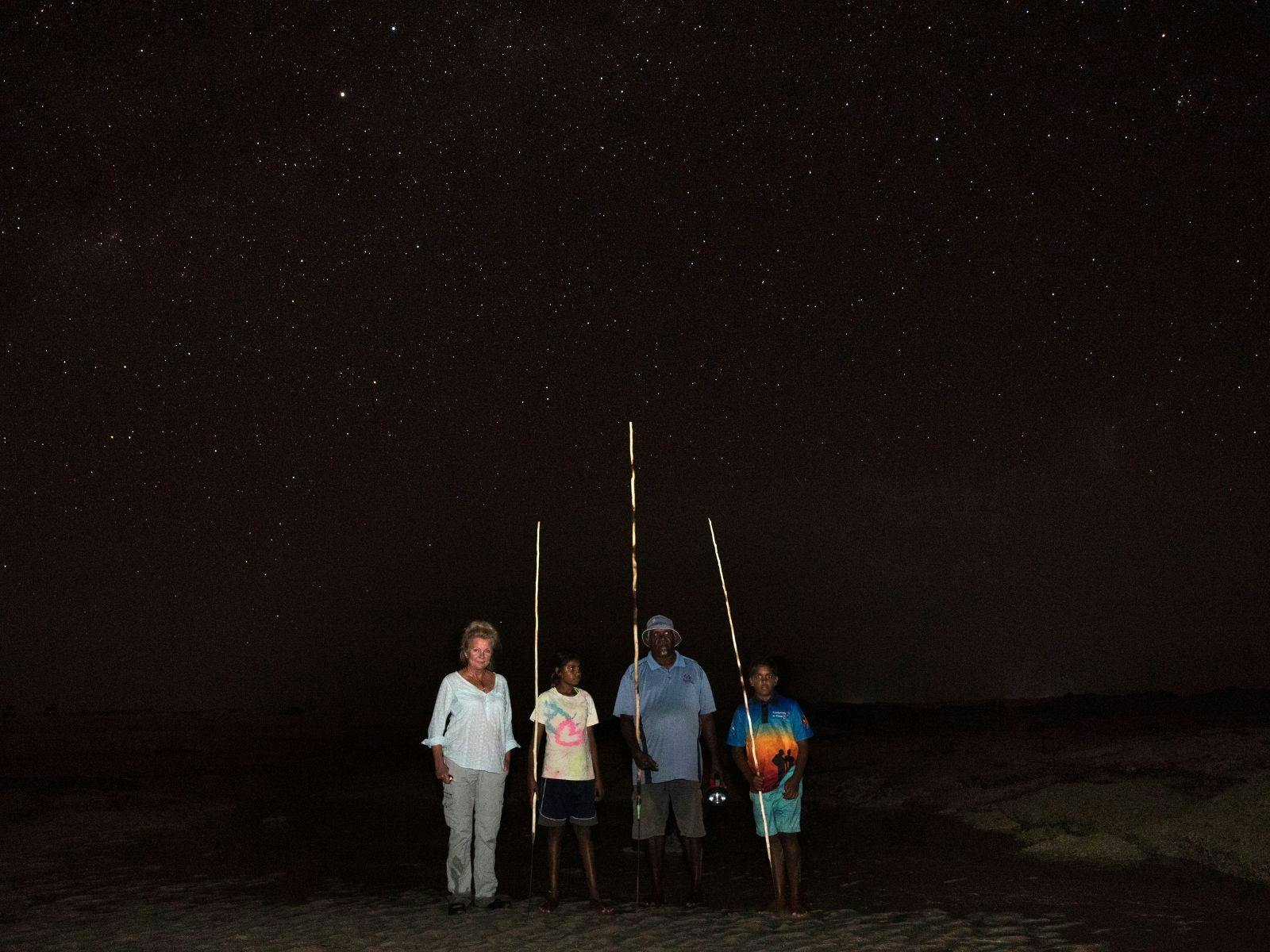 4 people standing on the beach with spears.