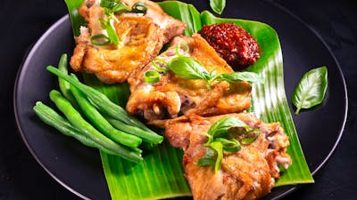 Ayam Penyet with sambal terasi and green beans served on a banana leaf