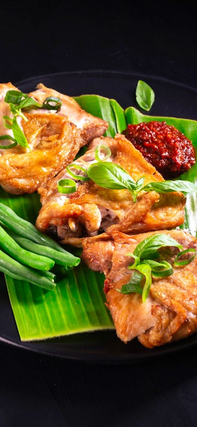 Ayam Penyet with sambal terasi and green beans served on a banana leaf