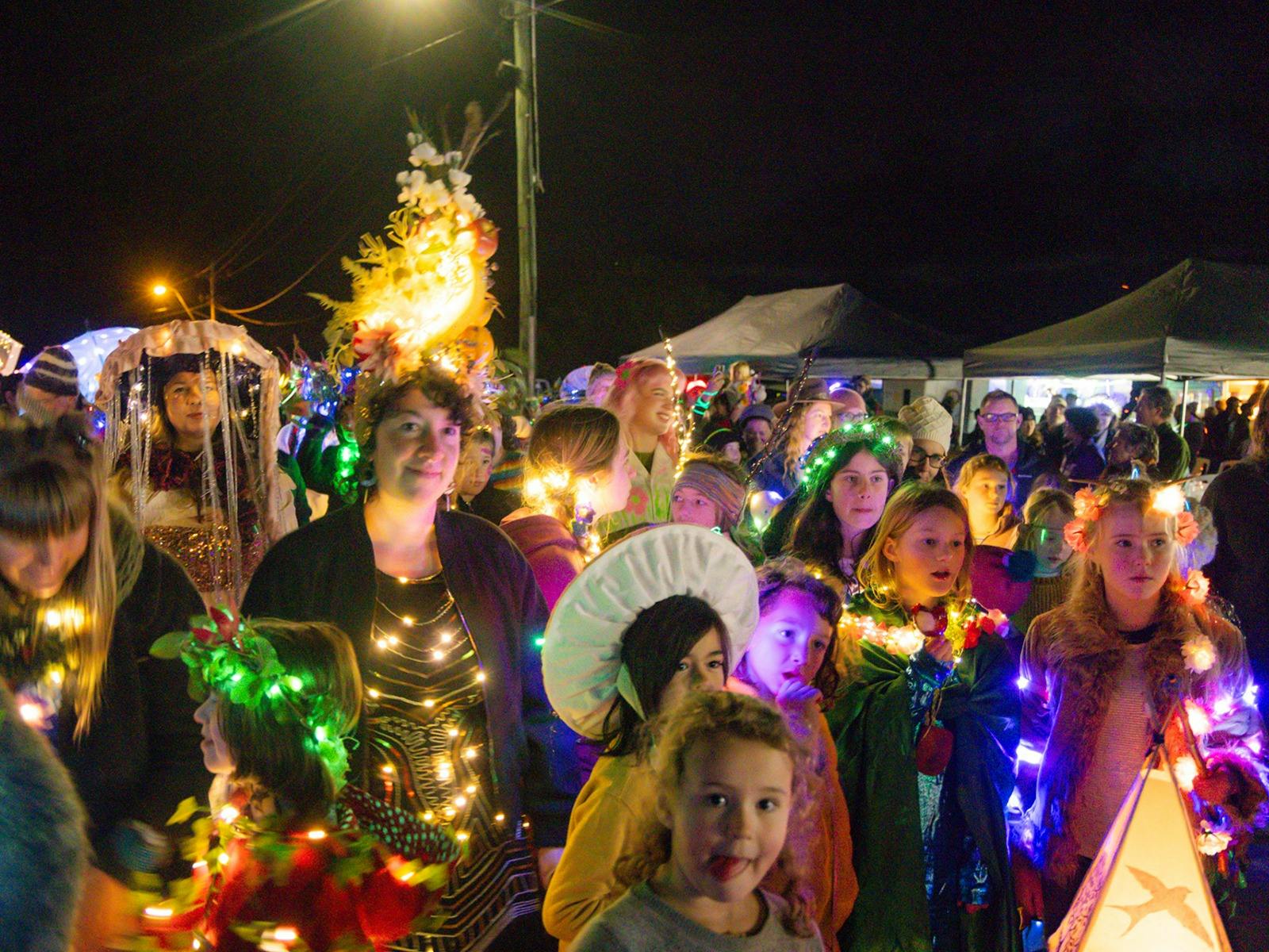 Families wearing illuminated costumes walk in The Light Parade.