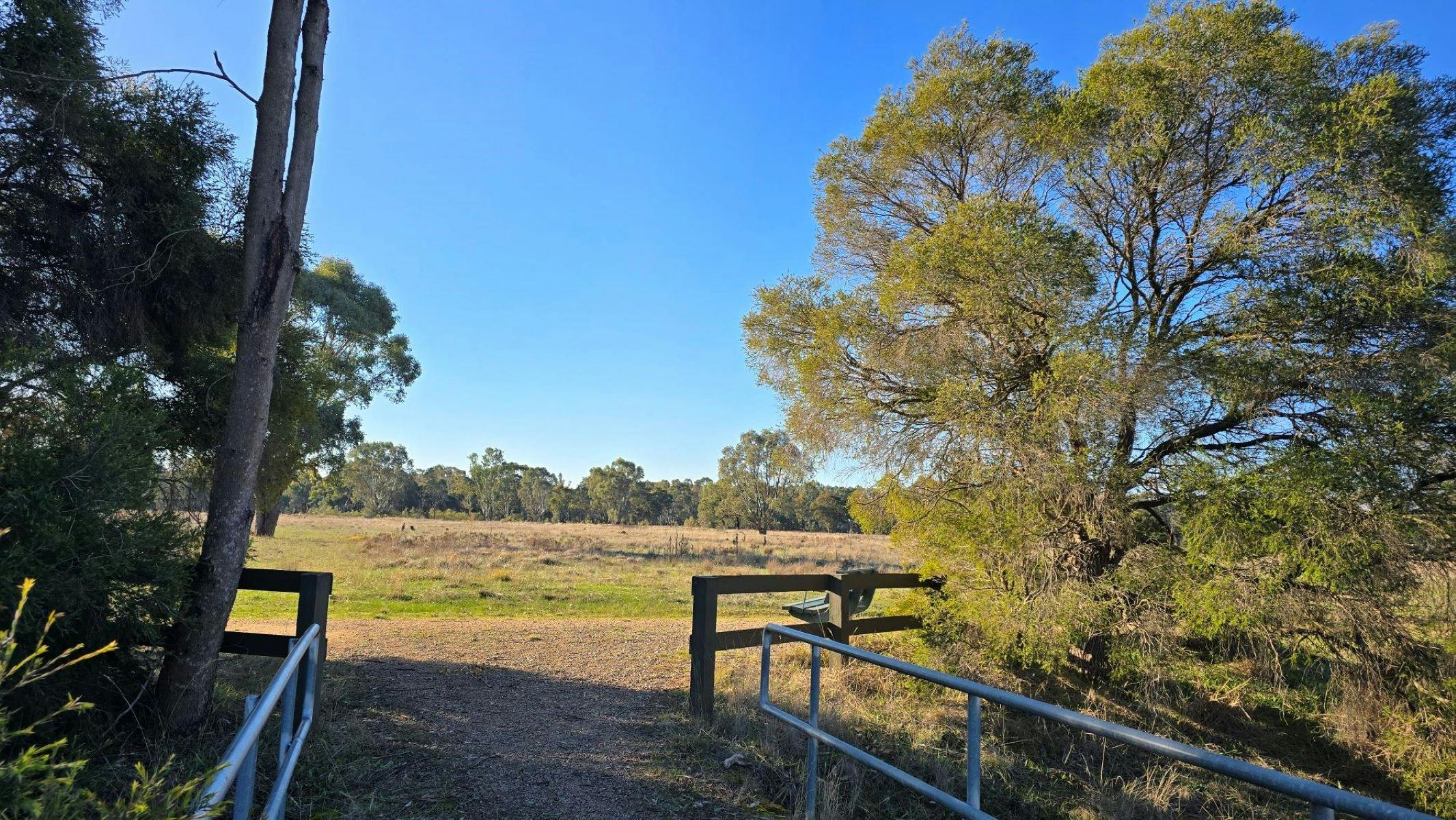 Bridge with gravel path leading into paddock with blue sky