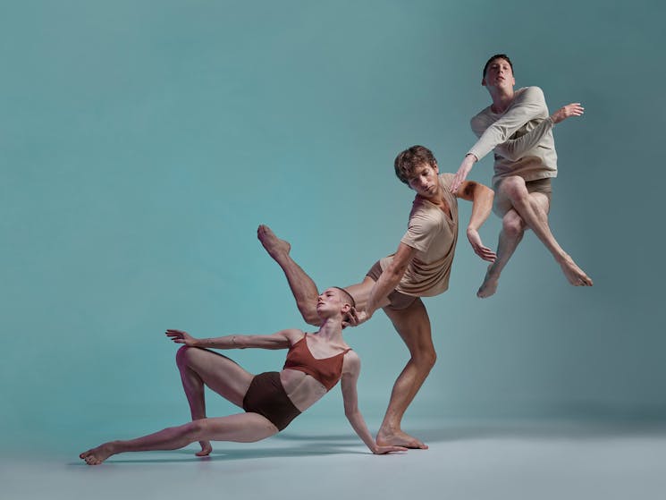 Three contemporary dancers are photographed in an ascending diagonal line on a pale blue background.