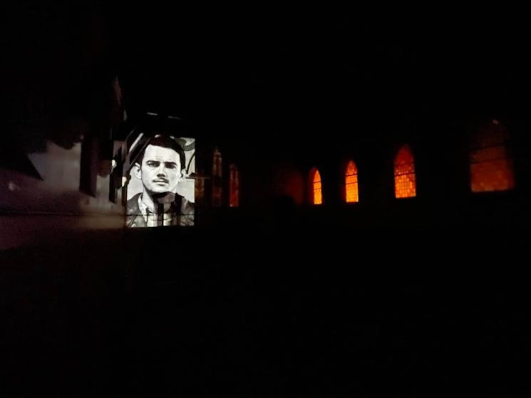 Picture of inside the chapel, it is dark with a projection of Leonard Keith Lawson on the wall
