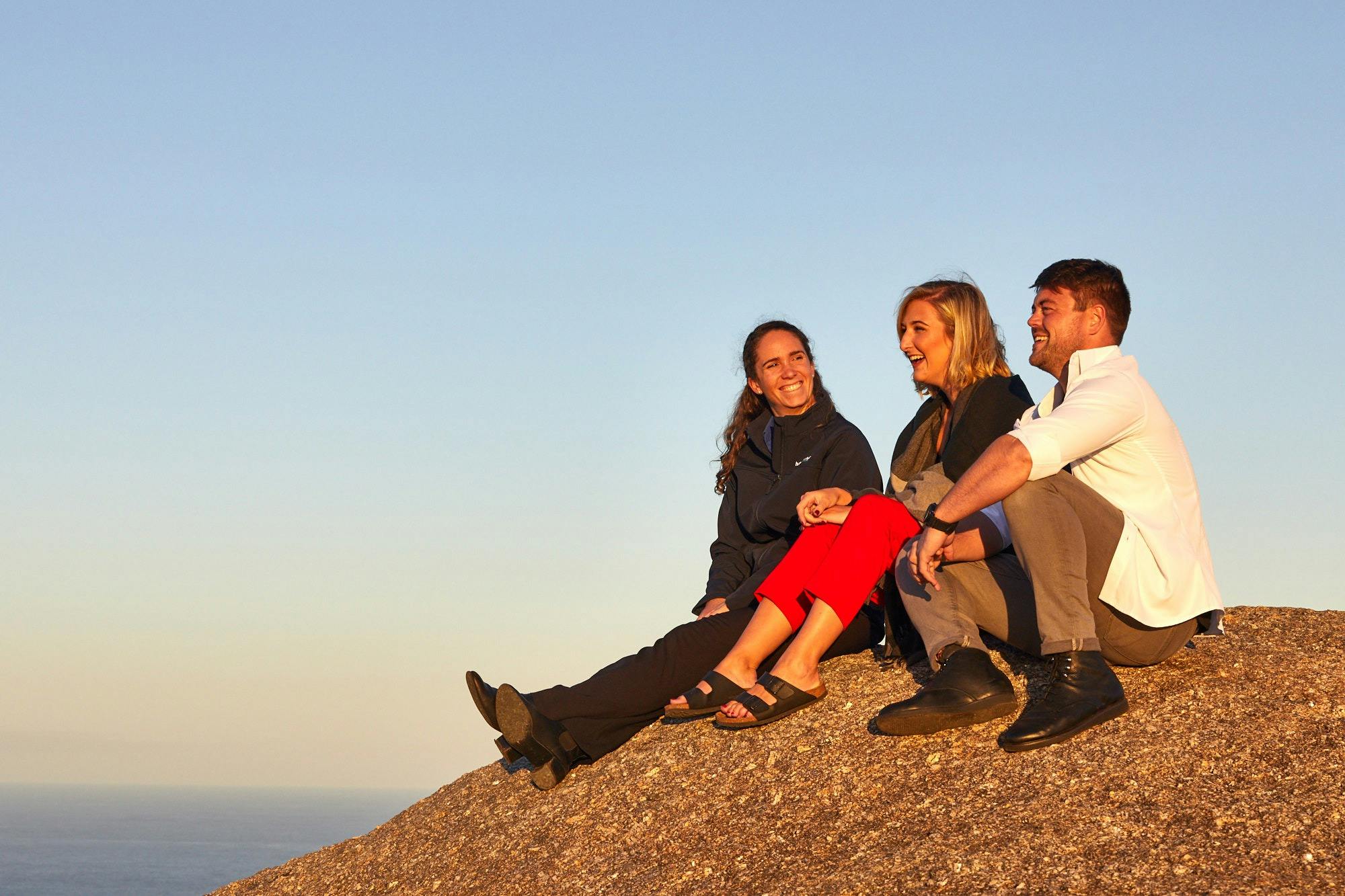 three people sitting on a rock with brilliant blue sky background