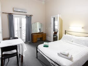 Interior of a double room with a queen-sized bed, dressing table, and balcony access.