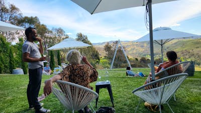 A man stands under an umbrella at a winery, seeking shelter from the rain.