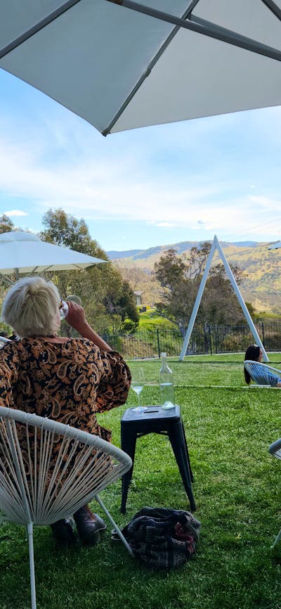 A man stands under an umbrella at a winery, seeking shelter from the rain.