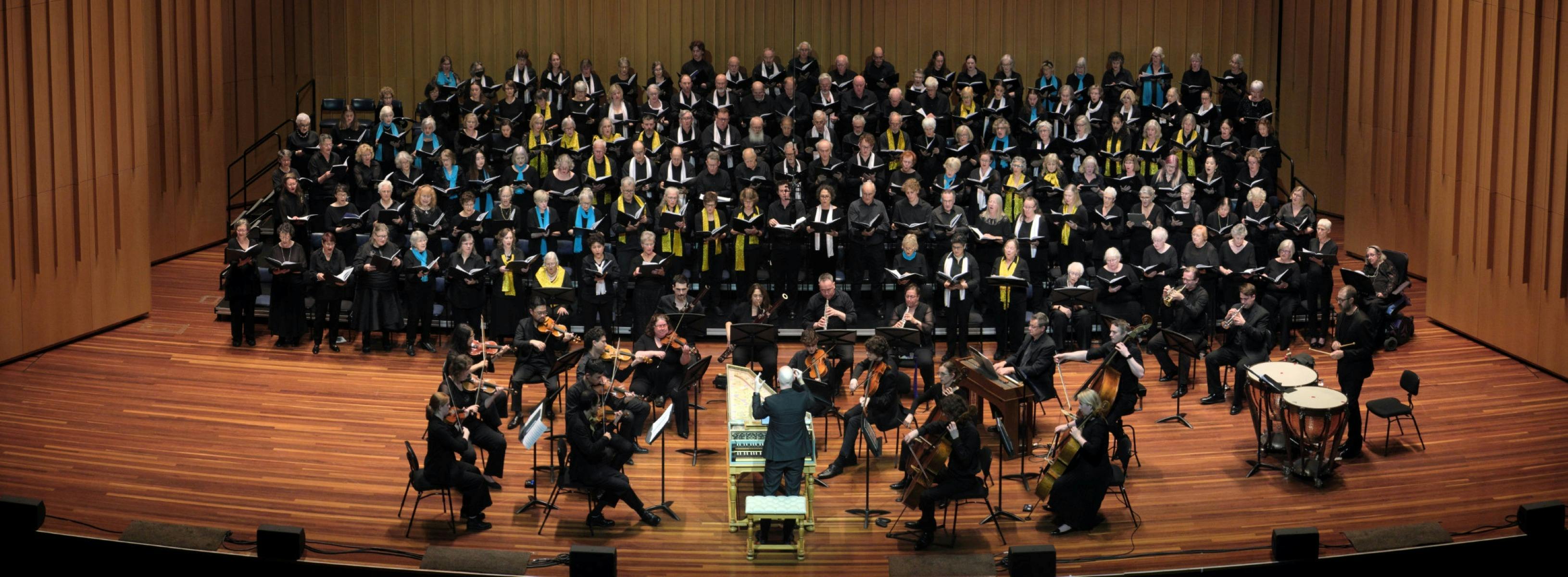 Choristers performing on stage with orchestra, conducted from a harpsichord by Erin Helyard