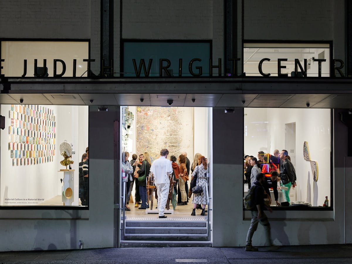 An art gallery with people inside it. Textural works line the walls and sculptures in amongst people
