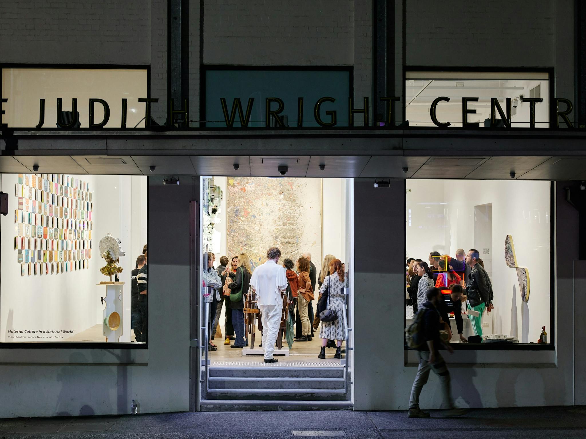 An art gallery with people inside it. Textural works line the walls and sculptures in amongst people An art gallery with people inside it. Textural works line the walls and sculptures in amongst people