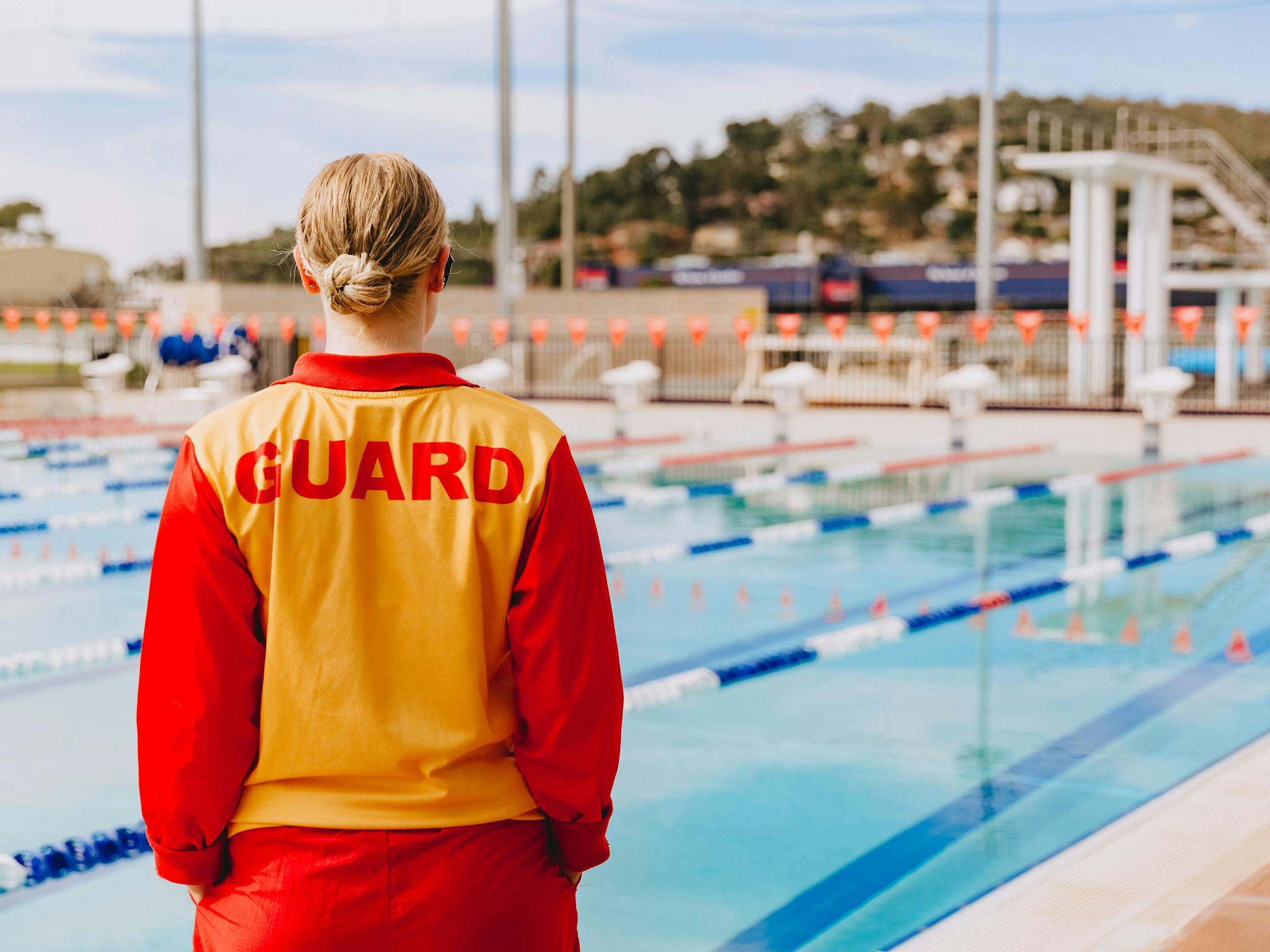 A life guard in uniform watches over the outdoor olympic pool