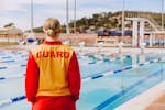 A life guard in uniform watches over the outdoor olympic pool