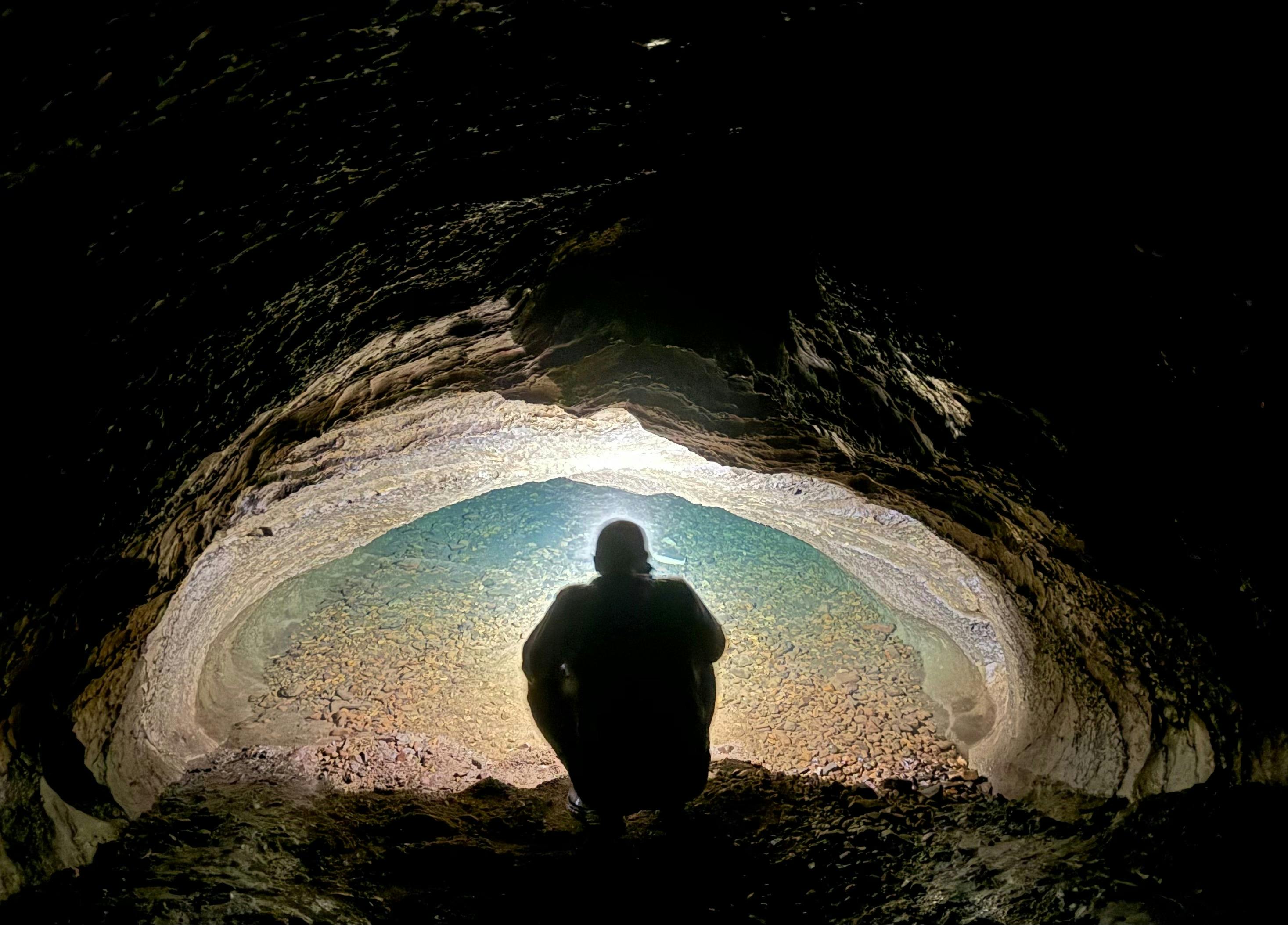A person looking into a water filled siphon in a cave.