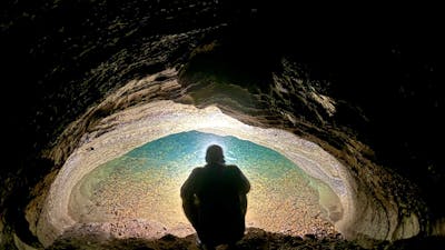A person looking into a water filled siphon in a cave.