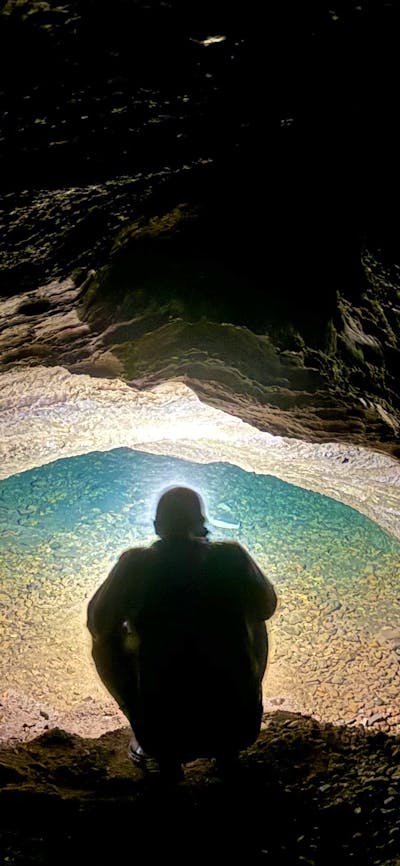 A person looking into a water filled siphon in a cave.