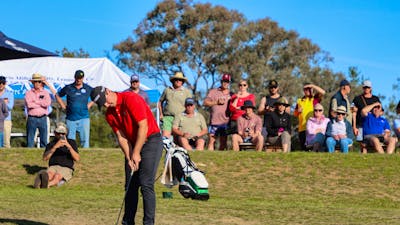 Male golfer putting in front of a crowd on a sand green
