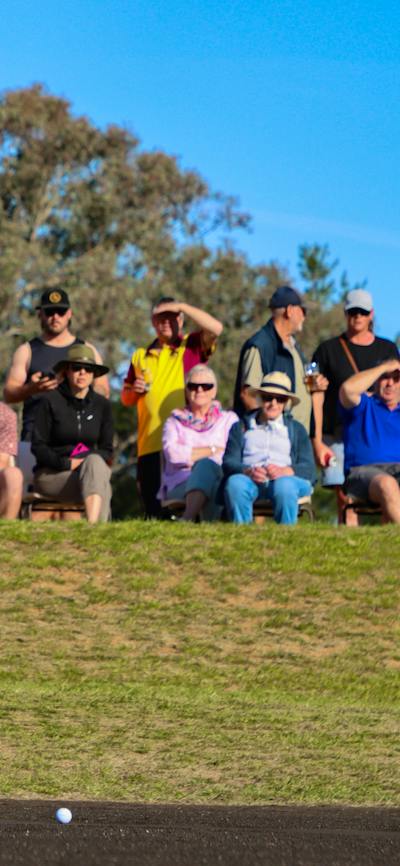 Male golfer putting in front of a crowd on a sand green