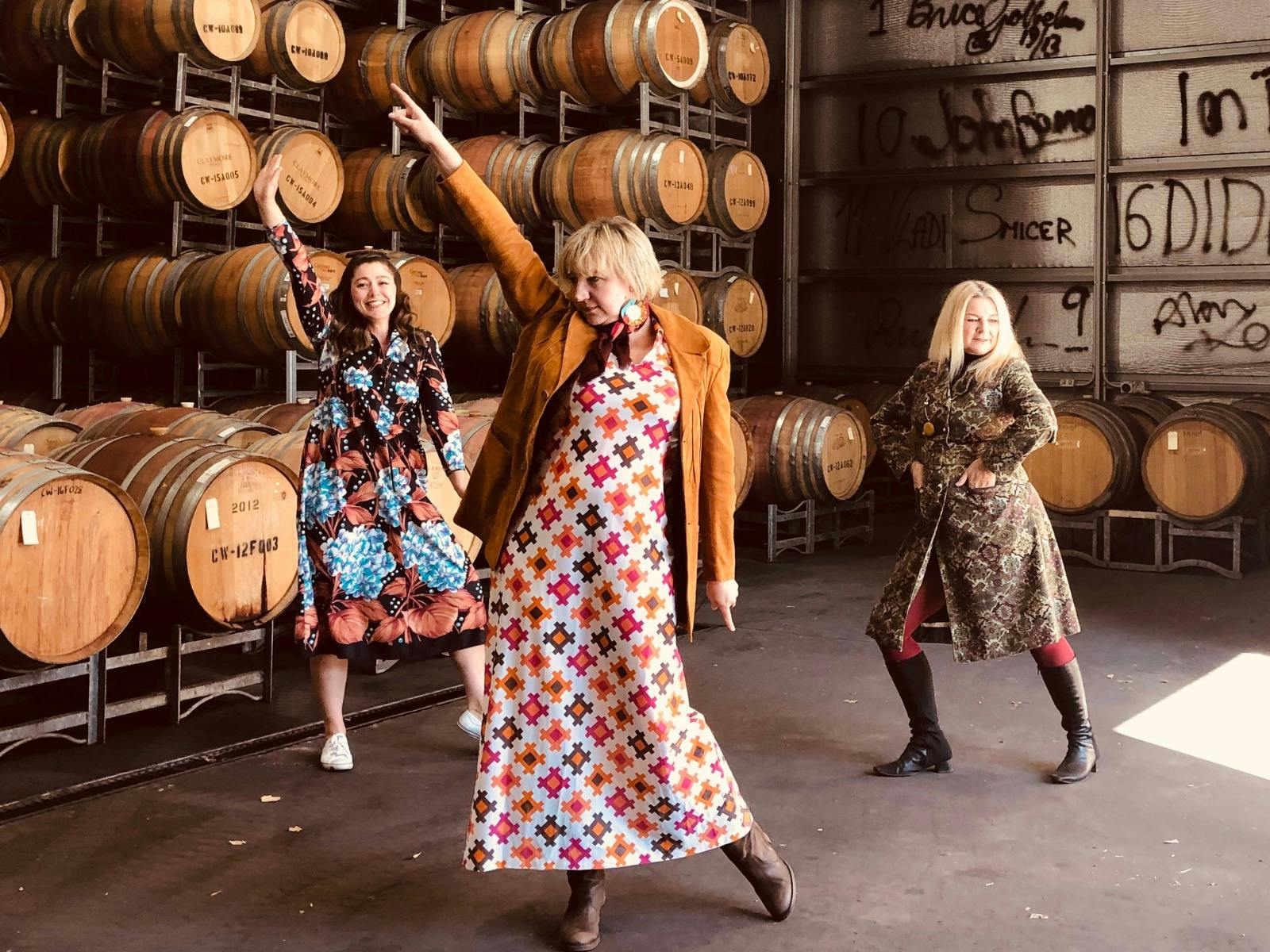 three women in vintage dresses dancing among barrels