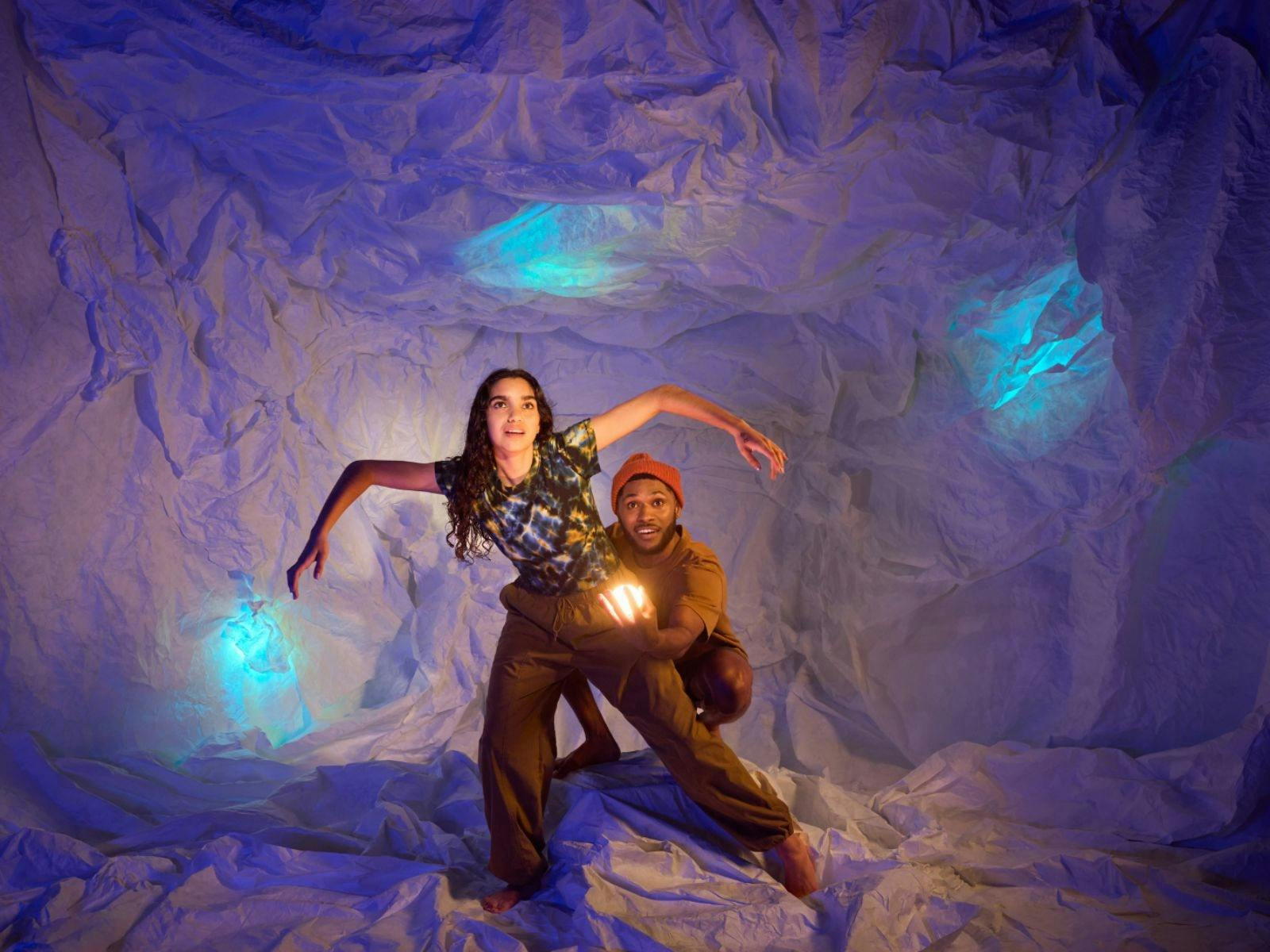 young female with arms out and man behind her holding a light in a cave environment