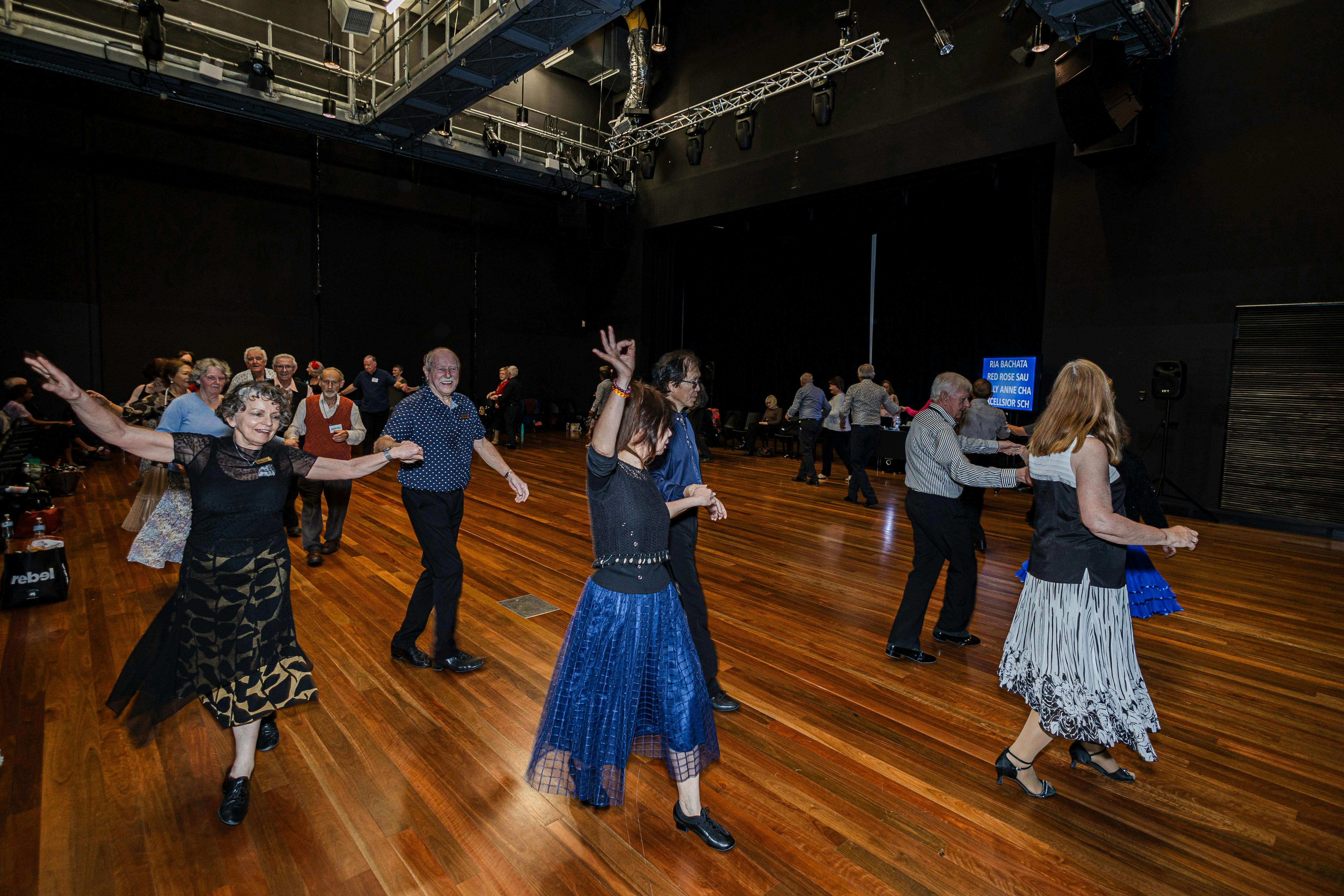 People dancing in a circle in a hall. Dancers are wearing blue clothing.