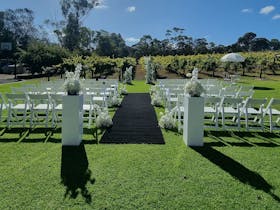 Outdoor ceremony setup with white chairs, on our grassed area in front of grape vines