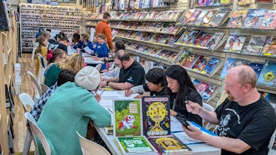 Adults and children sitting at tables in a comic shop drawing on paper