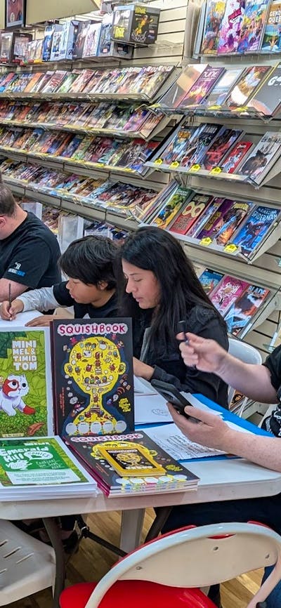 Adults and children sitting at tables in a comic shop drawing on paper