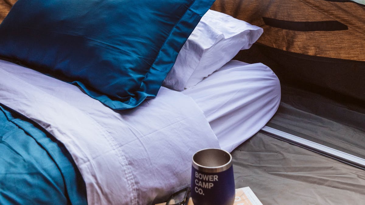 A mattress made up with blue and white sheets and bedding in a tent