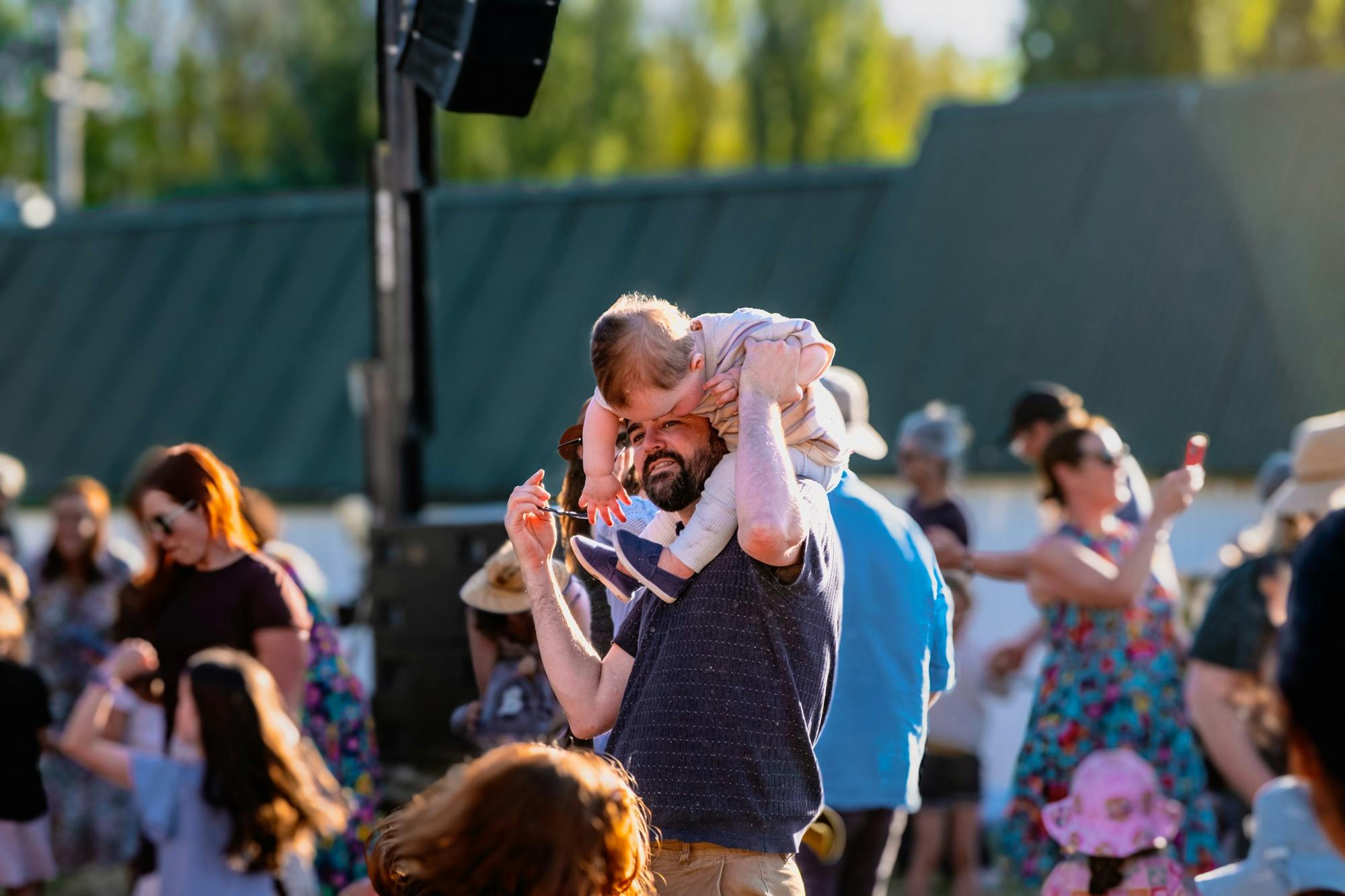 Parent lifting small child on his shoulders to dance and enjoy Live at Lanyon