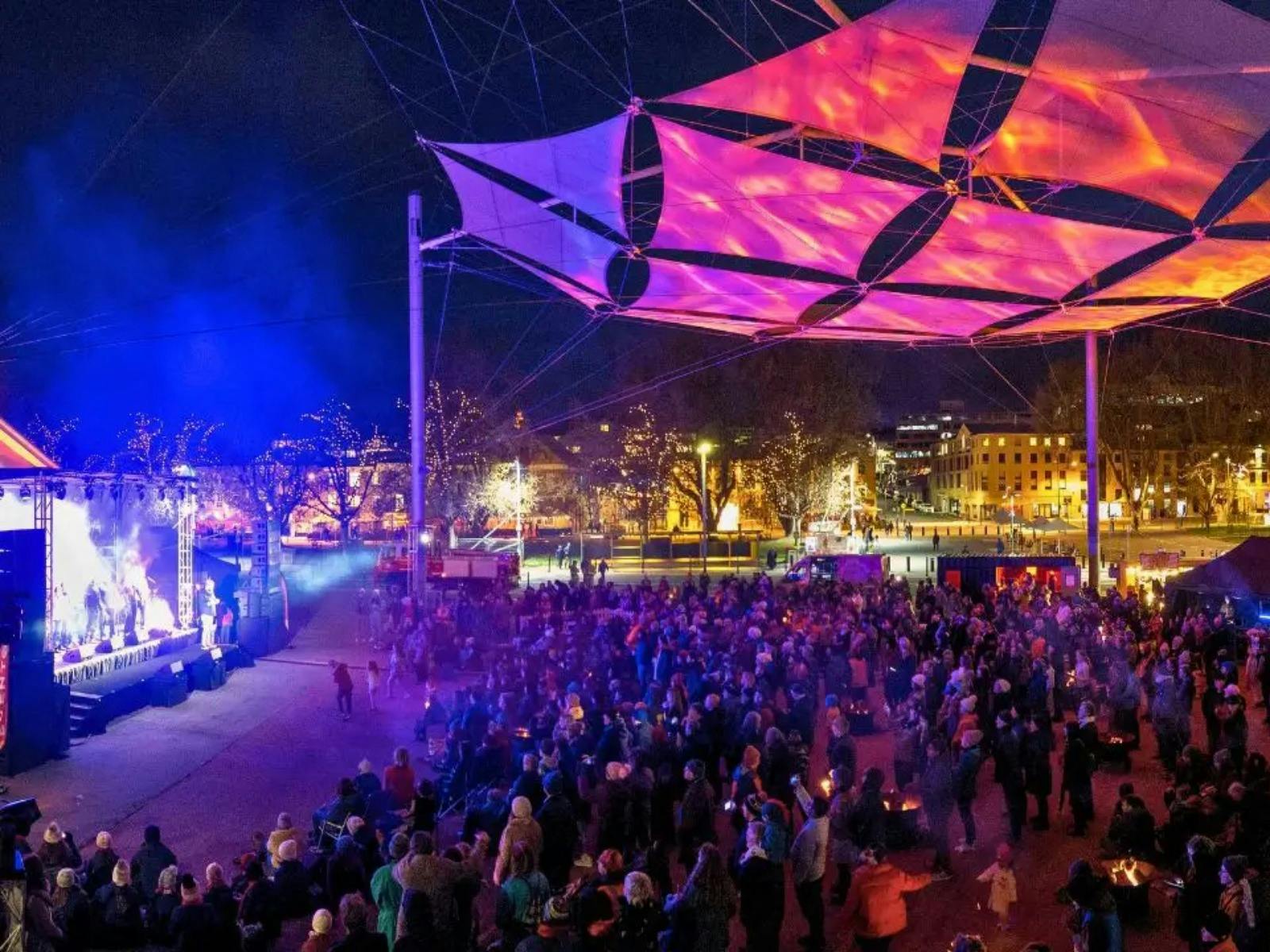 Large crowd at a night concert or festival, illuminated by blue and pink lights.