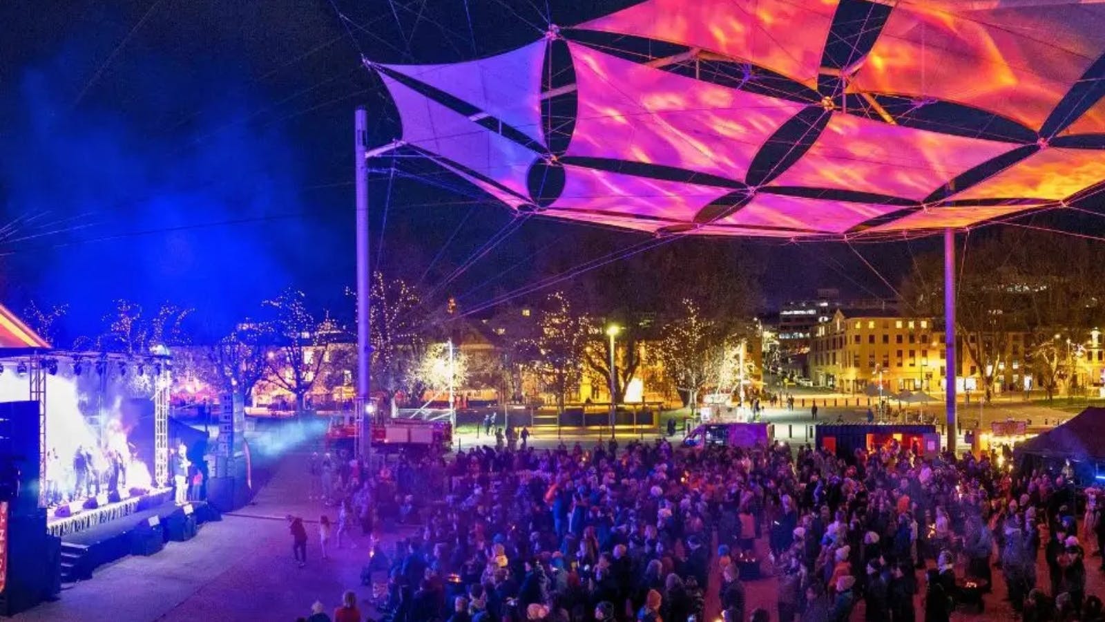 A vibrant night festival under a glowing canopy with a band on stage.